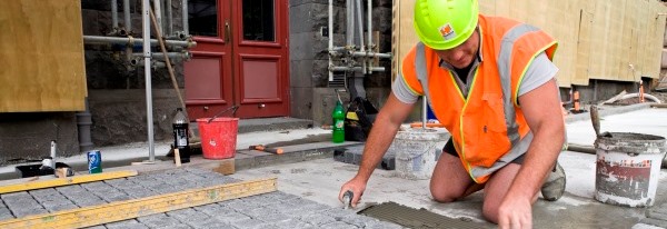 A worker in a hi-vis vest kneels while paving stones.